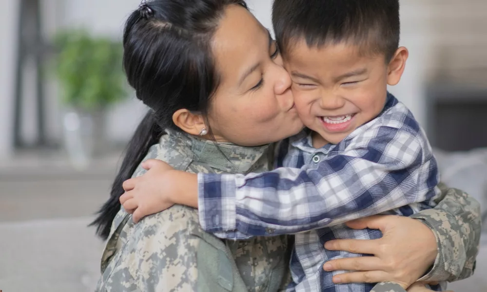 woman in military uniform hugging and kissing her child