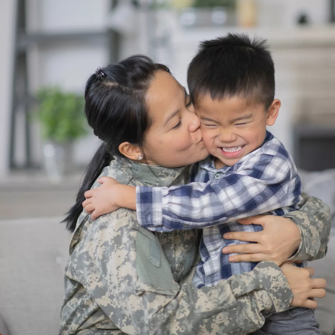 woman in military uniform hugging and kissing her child